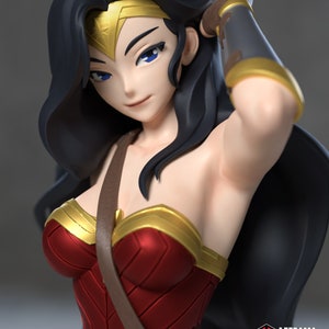 Puede incluir: Primer plano de una figura de Wonder Woman con un corpiño rojo y dorado, una correa de cuero marrón y una capa negra. Su cabello es largo y negro, y tiene ojos azules. La figura está hecha de plástico y mide aproximadamente 30 cm de alto.