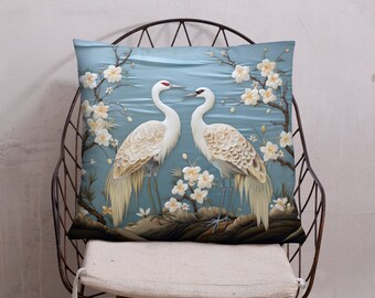 May include: A decorative pillow with a blue background featuring two white cranes with detailed embroidery. The cranes are surrounded by white flowers and green leaves.