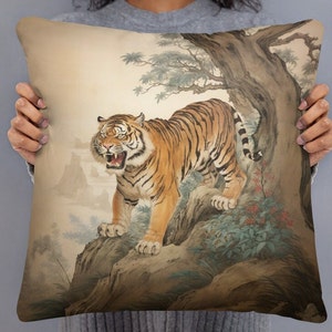 May include: A beige throw pillow featuring a watercolour illustration of a tiger roaring in a woodland setting. The tiger is orange and black with white stripes. The background is a light brown with green foliage and a large tree trunk.