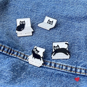 May include: Four enamel pins with black cat designs on white laptops. One pin says "DON'T WORRY I'M FROM TECH SUPPORT", another says "I'M A PURRGRAMMER", a third says "THINK BEFORE YOU CLICK", and the last says "WORKING FROM HOME". The pins are on a blue denim background.