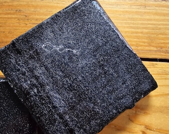 May include: A black square coaster with a slightly textured surface. The coaster is made of a glossy material and has a subtle sheen.