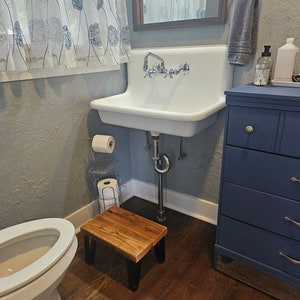 May include: A white porcelain sink with a chrome faucet and a wooden stool in a bathroom with blue walls and a dark wood floor.