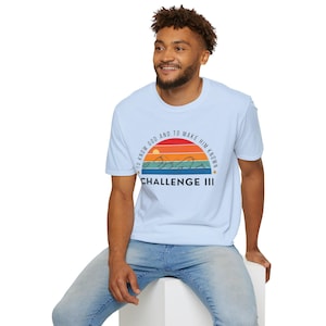 May include: Light blue t-shirt with a colorful graphic of a sunset over mountains. The text "TO KNOW GOD AND TO MAKE HIM KNOWN" arches above the design, with "CHALLENGE III" below. The shirt is made of a soft material.