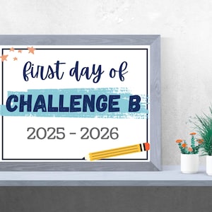 May include: A framed print with the text "first day of CHALLENGE B 2025-2026." The text is in a mix of fonts and colors, with a blue banner and a yellow pencil illustration. The frame is gray.