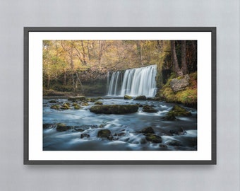 May include: A photograph of a waterfall cascading over rocks in a forest. The water is flowing over the rocks and creating a misty spray. The trees are in the background and the leaves are changing color.