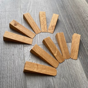 May include: A set of ten wooden door stops in a light brown colour arranged in a semi-circle on a grey wood floor.