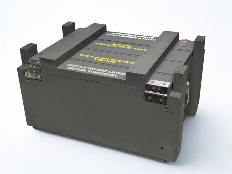 K&ouml;nnte beinhalten: Eine olivgr&uuml;ne, rechteckige Munitionskiste aus Holz mit Metallscharnieren und verst&auml;rkten Ecken. Auf der Oberseite befindet sich gelber Schablonentext 5.56 X 45 MM NATO M193 1200 RDS und TIGHTLY SECURE LATCH BEFORE TRANSPORT in wei&szlig;er Schrift.