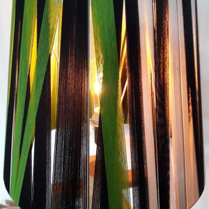 May include: A lampshade made of woven black, white, and green yarn. The lampshade is cylindrical and has a geometric pattern.