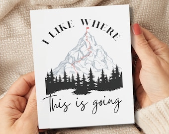 May include: A white card with a black and white illustration of a mountain with a red flag at the top. The text "I like where this is going" is printed on the card.