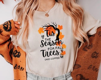 May include: A beige t-shirt with a black and orange graphic that says "Tis the season for fall trees (and coffee)". The graphic features a tree with leaves and a cup of coffee.