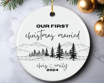 Puede incluir: Adorno navideño de cerámica blanca con texto negro que dice "Nuestra primera Navidad casados" con una cordillera y pinos en el fondo. Los nombres "Chris" y "Emily" están escritos debajo de las montañas con un símbolo de corazón y el año "2024".