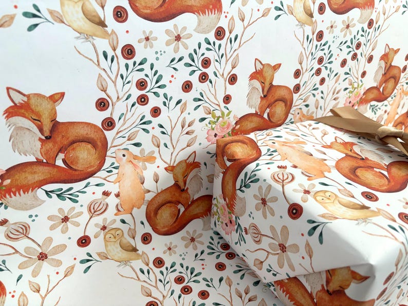 May include: White wrapping paper with a repeating pattern of foxes, owls, and rabbits among flowers and foliage. The gift wrap is tied with a gold ribbon. The overall design has a watercolor effect.