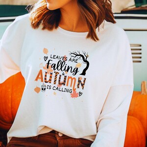 May include: White long-sleeve sweatshirt with a graphic print of leaves falling and the text "Leaves are falling & autumn is calling".
