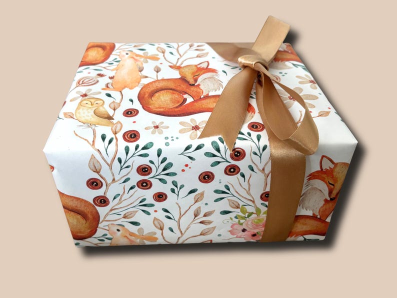 May include: A wrapped gift box featuring a woodland animal print with foxes, owls, and rabbits. The gift is wrapped in white paper with a repeating pattern of forest creatures and floral accents. A gold satin ribbon is tied in a bow.