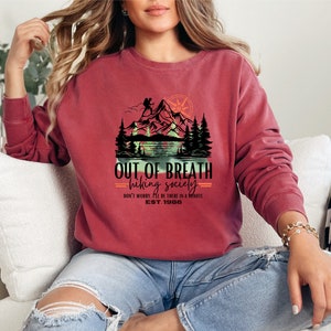 May include: Crimson red sweatshirt with a graphic of a mountain scene and the text "OUT OF BREATH hiking society DON'T WORRY. I'LL BE THERE IN A MINUTE EST. 1986".