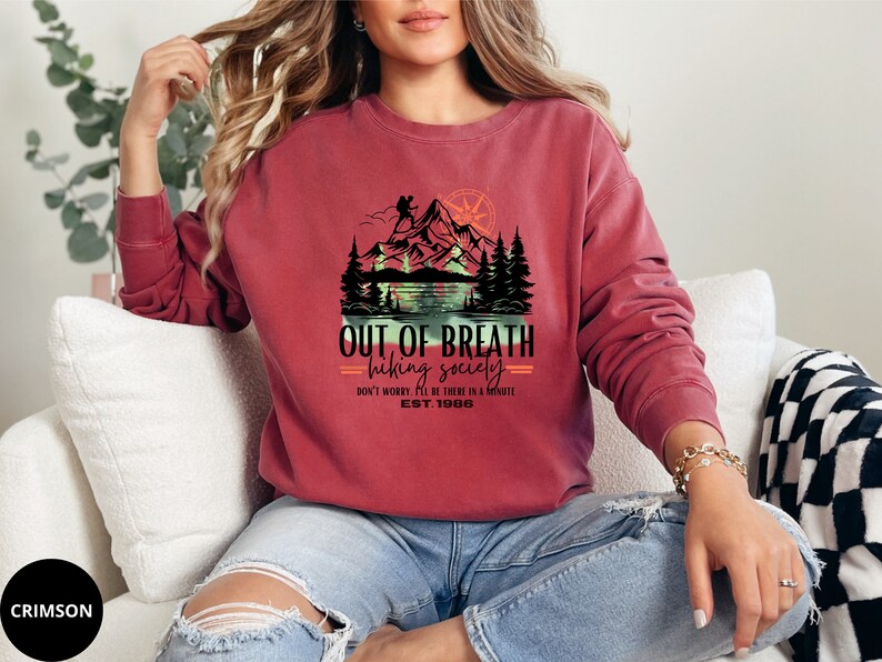 May include: Crimson red sweatshirt with a graphic of a mountain scene and the text "OUT OF BREATH hiking society DON'T WORRY. I'LL BE THERE IN A MINUTE EST. 1986".