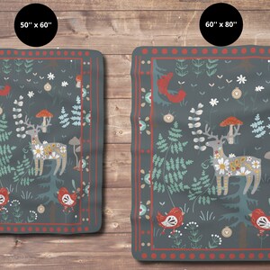 May include: A dark blue fleece blanket with a whimsical forest scene featuring a deer, mushrooms, birds, and flowers. The blanket has a red and white border.