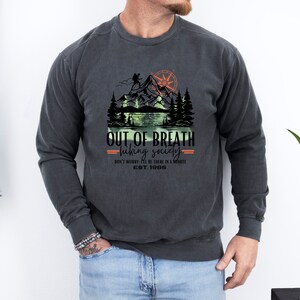 May include: A dark gray sweatshirt with a vintage-style graphic of a mountain scene with a hiker, a compass, and a lake. The text "OUT OF BREATH hiking society DON'T WORRY BE THERE IN A MINUTE EST. 1985" is printed below the graphic.