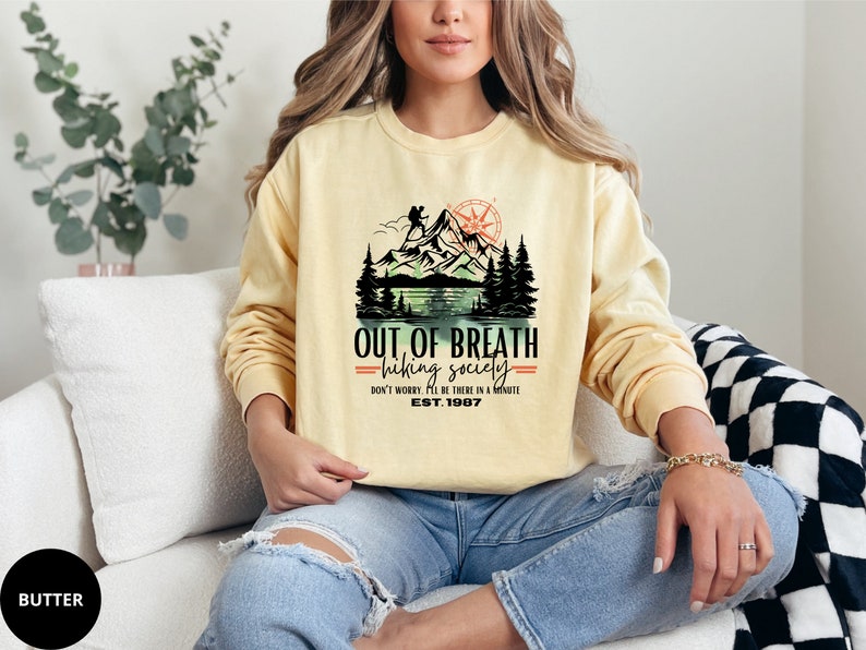 May include: A yellow sweatshirt with a graphic print of a mountain scene and the text "OUT OF BREATH =hiking society= DON'T WORRY. I'LL BE THERE IN A MINUTE EST. 1987"