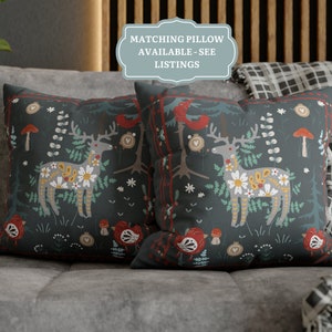 May include: Two decorative throw pillows with a dark blue background and a colorful Scandinavian-inspired pattern featuring a deer, flowers, and mushrooms. The text "Matching Pillow Available - See Listings" is on a blue label.