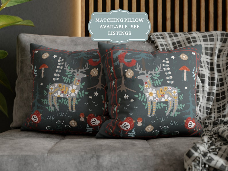 May include: Two decorative throw pillows with a dark blue background and a colorful Scandinavian-inspired pattern featuring a deer, flowers, and mushrooms. The text "Matching Pillow Available - See Listings" is on a blue label.
