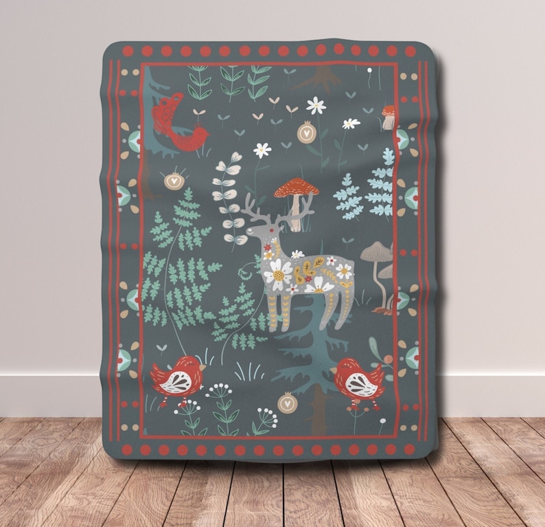 May include: A dark blue throw blanket with a red and white border. The blanket features a whimsical forest scene with a deer, birds, mushrooms, and flowers.