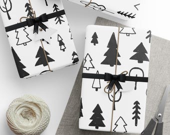 May include: Two white gift boxes wrapped in black and white patterned paper with a black and white tree design. The boxes are tied with black ribbon and twine. One box is on a gray fabric surface and the other is on a white surface.