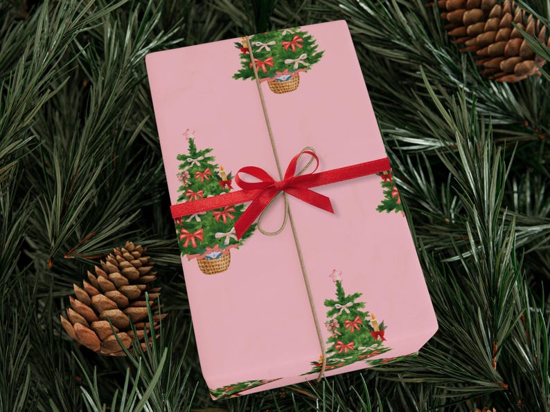 以下が含まれることがあります： 赤いリボンと紐で結ばれた、ピンク色の包装紙。クリスマスツリーが繰り返し描かれており、赤いリボンとオーナメントで飾られています。