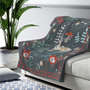 May include: A soft, dark blue throw blanket with a whimsical forest scene featuring a deer, mushrooms, and floral patterns. The blanket has a red and white border with a repeating pattern of dots. The blanket measures 50 inches by 60 inches.