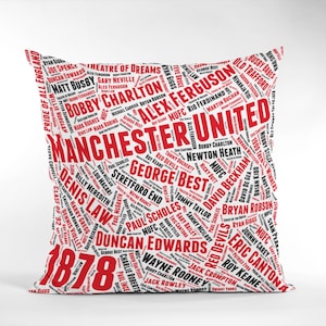 Könnte beinhalten: Quadratisches weißes Kissen mit einem roten und schwarzen Textdesign. Die Worte "Manchester United" sind prominent dargestellt, umgeben von Namen wie George Best, David Beckham und Alex Ferguson. Das Jahr "1878" ist ebenfalls sichtbar.