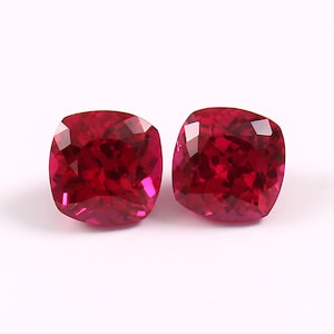 Könnte beinhalten: Zwei rote Kissen-Schliff-Edelsteine, wahrscheinlich Rubine, auf weißem Hintergrund.