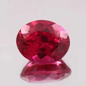 May include: A vibrant red gemstone with a round cut and a high polish. The gemstone is set against a white background.