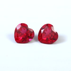 Peut inclure: Deux pierres précieuses rouges vives en forme de cœur, à facettes. Les pierres sont présentées sur un fond blanc. Les facettes captent la lumière, créant un effet scintillant. Pour bijoux ou autres créations.