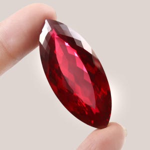 May include: A large, deep red, faceted gemstone with a marquise cut.
