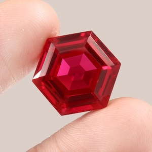 Puede incluir: Una piedra preciosa de color rojo intenso con un corte hexagonal y un diseño facetado.