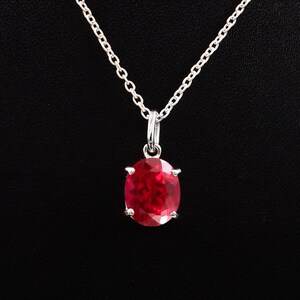 May include: A silver necklace featuring a large, oval red gemstone pendant. The gemstone is set in a silver bezel and suspended from a delicate silver chain. The background is a solid black.