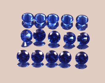 May include: A collection of 15 round, faceted, sapphire blue gemstones. The gemstones are arranged in three rows of five, with each row slightly offset from the one above it.