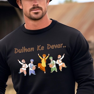 May include: Black sweatshirt featuring a graphic of dancing figures in traditional attire. The figures are in various colors, with the text "Dulhan Ke Devar.." in brown. The sweatshirt has long sleeves and a crew neck.