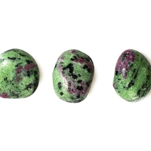 Può includere: Tre pietre rotonde di gemma verde, rosa e nera. Le pietre sono lisce e levigate.