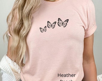 May include: A pink t-shirt with a row of four black butterfly silhouettes. The shirt has the text "Heather Peach" printed on the bottom.