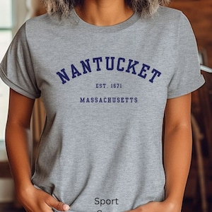 Könnte beinhalten: Ein graues T-Shirt mit einem marineblauen Aufdruck, auf dem "NANTUCKET EST. 1671 MASSACHUSETTS" steht.