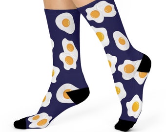 Puede incluir: Un par de calcetines azules con un patrón de huevos fritos blancos. Los calcetines se muestran en los pies de una modelo.