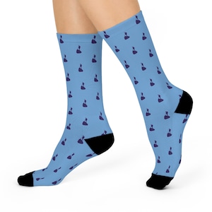 May include: Light blue socks with a repeating pattern of dark purple figures. The socks have black heels and toes. These socks are a fun and stylish accessory.
