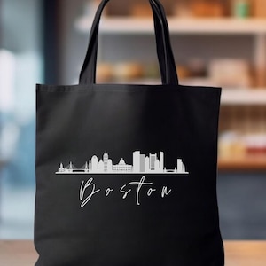 Puede incluir: Bolsa de tela negra con una silueta blanca del horizonte de Boston y la palabra "Boston" en escritura blanca.