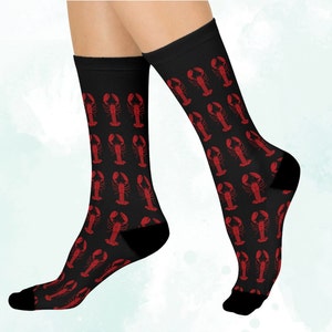 May include: A pair of black socks with a red lobster print. The socks are shown on a model's legs.
