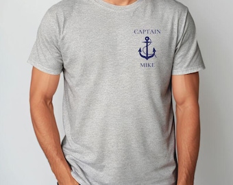 May include: Sport grey t-shirt with a crew neck. The shirt features a navy blue anchor graphic with the words "CAPTAIN" above and "MIKE" below. The shirt is made of a soft, comfortable material.