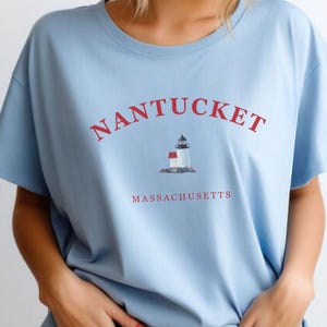 Könnte beinhalten: Ein hellblaues T-Shirt mit einer roten Grafik eines Leuchtturms und dem Text "NANTUCKET MASSACHUSETTS".