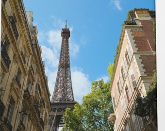 May include: A view of the Eiffel Tower in Paris, France, seen from a narrow street between two buildings. The buildings are old and have a classic Parisian architecture. The sky is blue and there are some clouds.