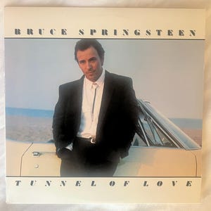 May include: Album cover for Bruce Springsteen's "Tunnel of Love." The image features Springsteen in a black suit, leaning against a car. The album title and artist's name are printed in a bold, sans-serif font.