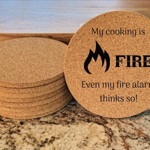 May include: Set of six round cork coasters with a black and white design. The coaster features a flame graphic and the text "My cooking is FIRE. Even my fire alarm thinks so!"